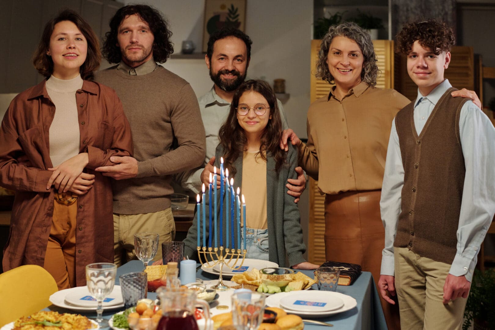 Family gathered around a table celebrating Hanukkah with lit menorah.